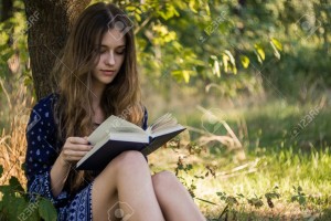 Girl sitting under a tree reading book in summer forest